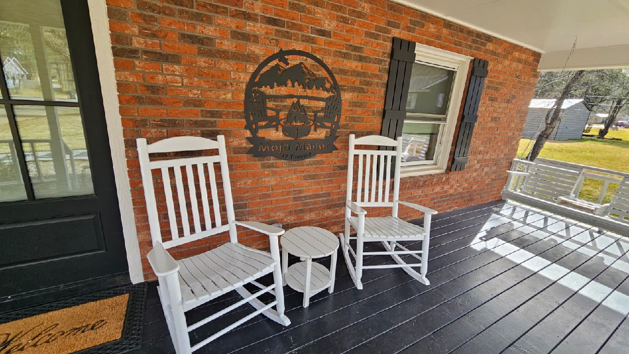 Mojo Manor front porch with white rocking chairs and custom metal sign